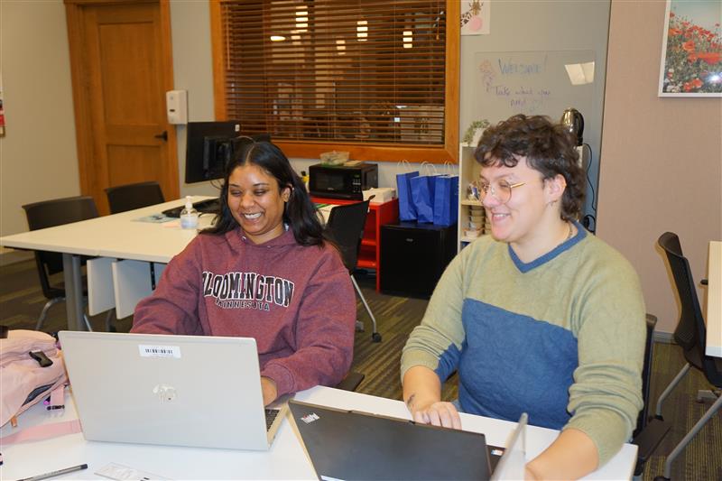 two people smiling sitting in front of laptops