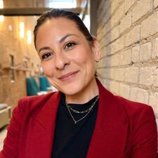Woman in red suit jacket leaning against a wall and smiling