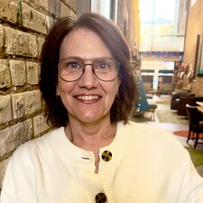 woman with short brown hair wearing a white sweater standing next to a wall and smiling