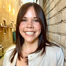 woman standing next to a brick wall with a tan jacket