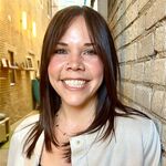 woman standing next to a brick wall with a tan jacket