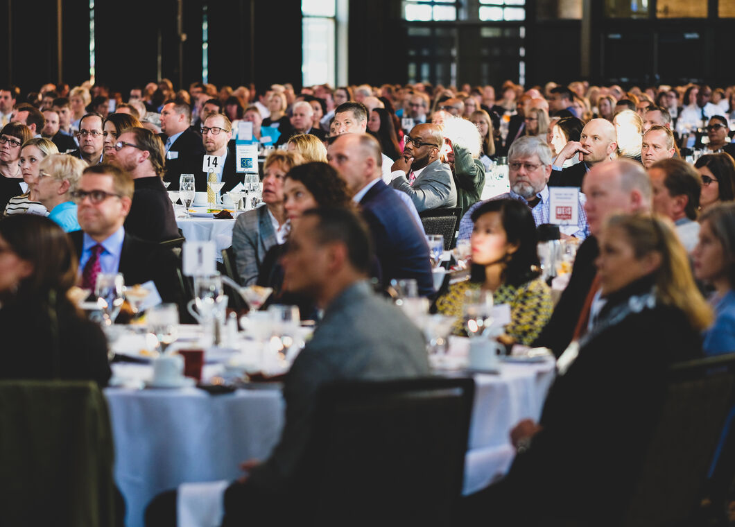 Many people seated at a number of round dining tables in a hotel space. 