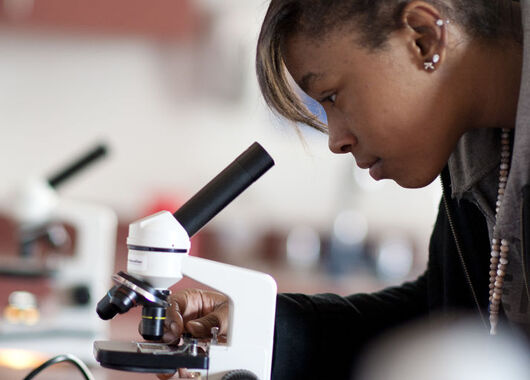 female student looking through a microscope lens