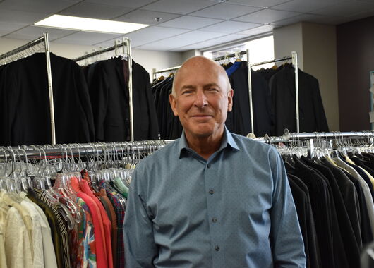 Man in blue shirt with racks of clothes behind him