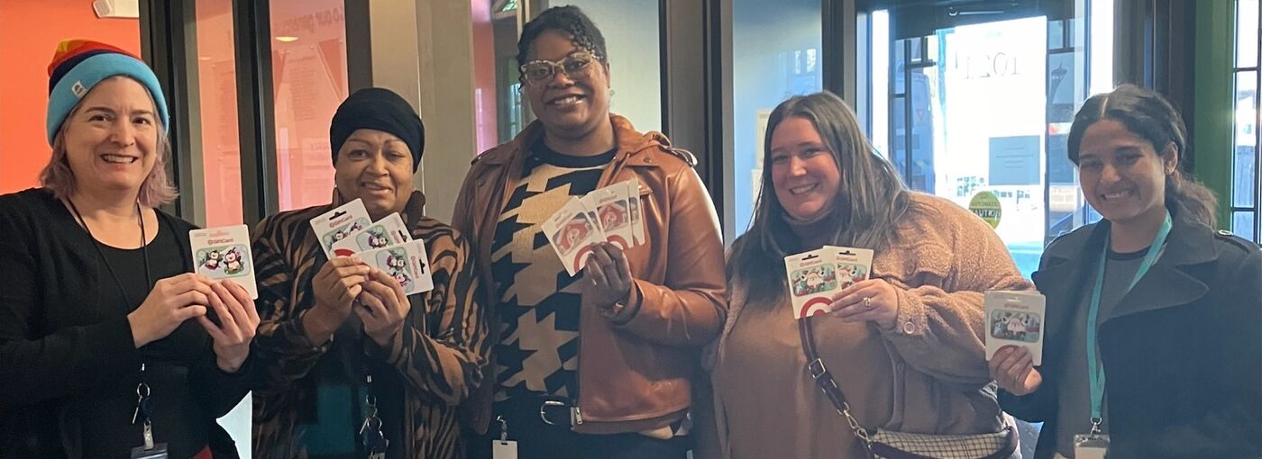 four people smiling holding gift cards to donate