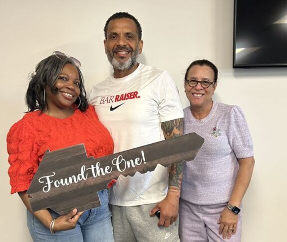 People smiling holdinga large wooden key with "Found the One!" written on it. 
