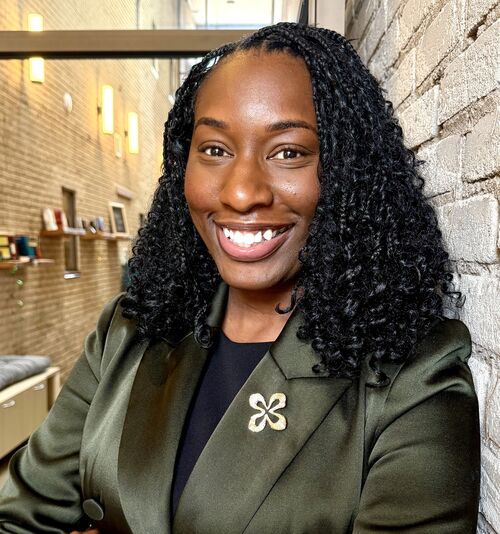Woman standing against a wall wearing a green blazer and smiling