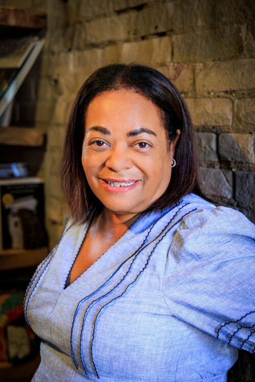 Woman in blue shirt standing next to brick wall and smiling