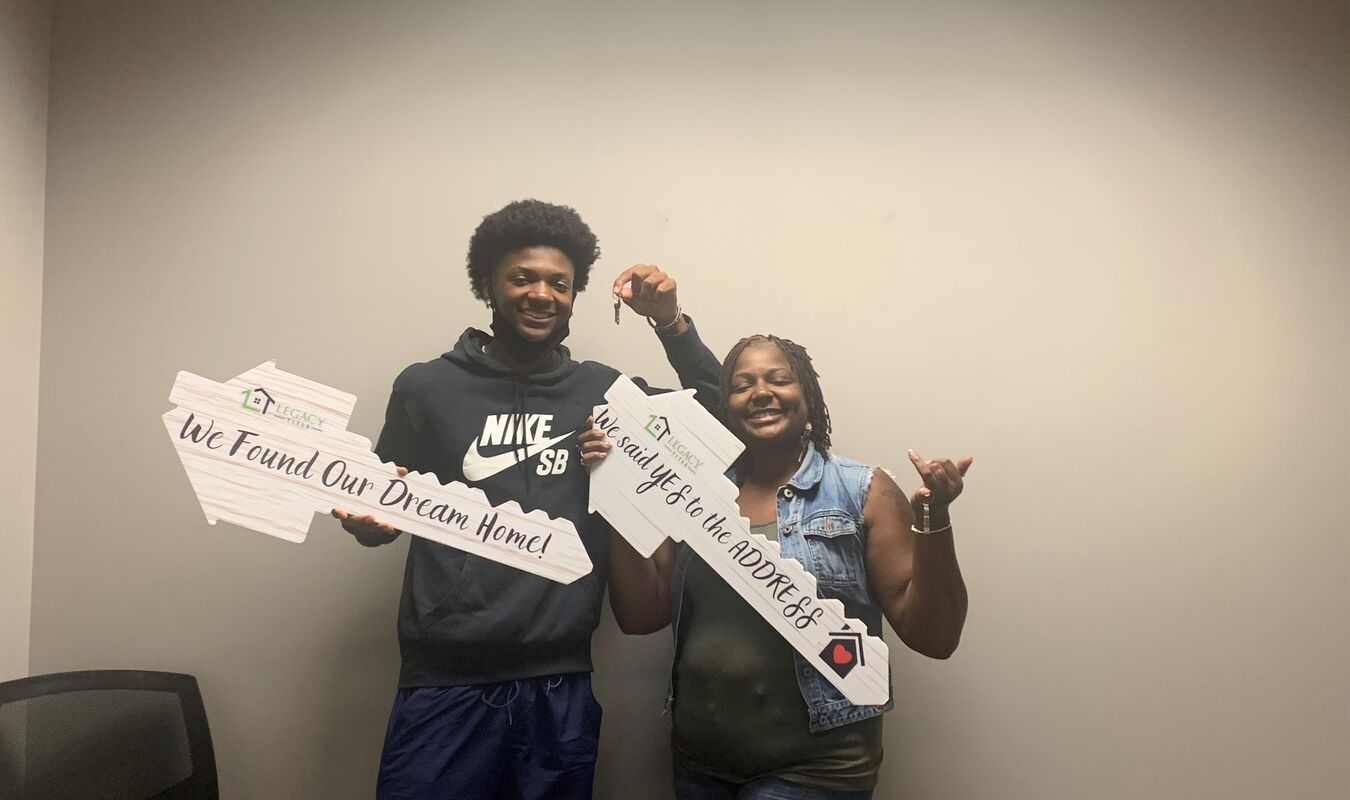 Two people smiling holding new home signs