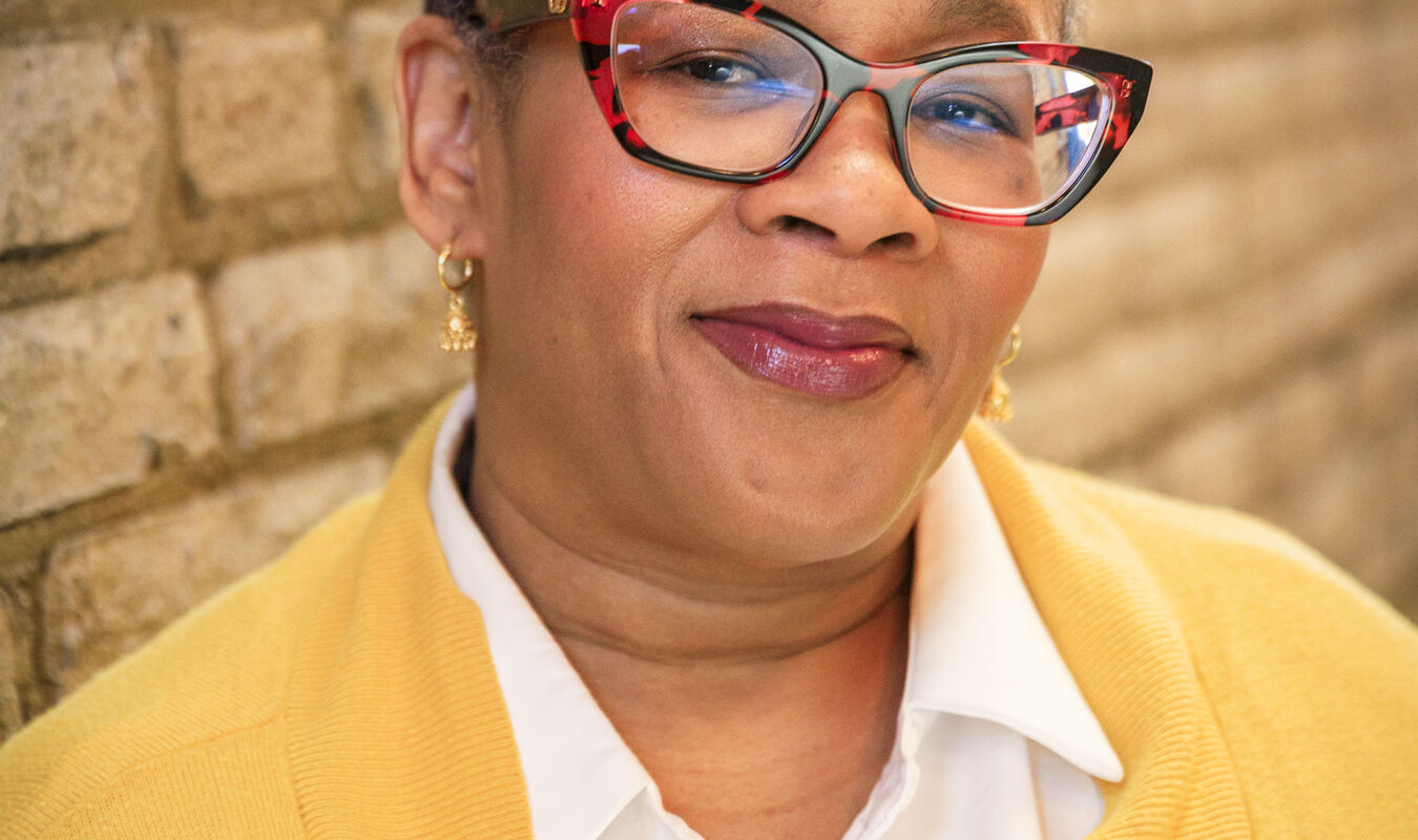 A headshot of Rashida Jackson wearing a yellow sweater standing against a brick wall 
