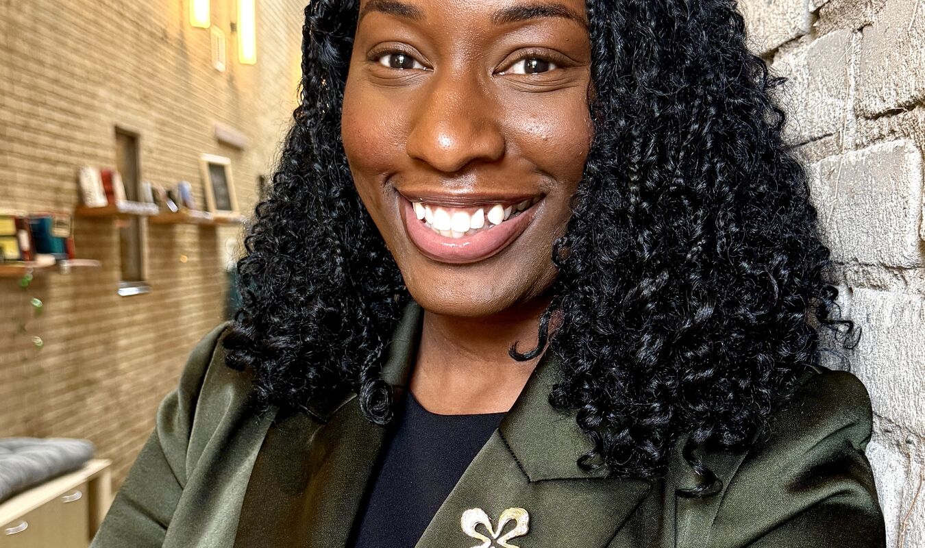 Woman standing against a wall wearing a green blazer and smiling