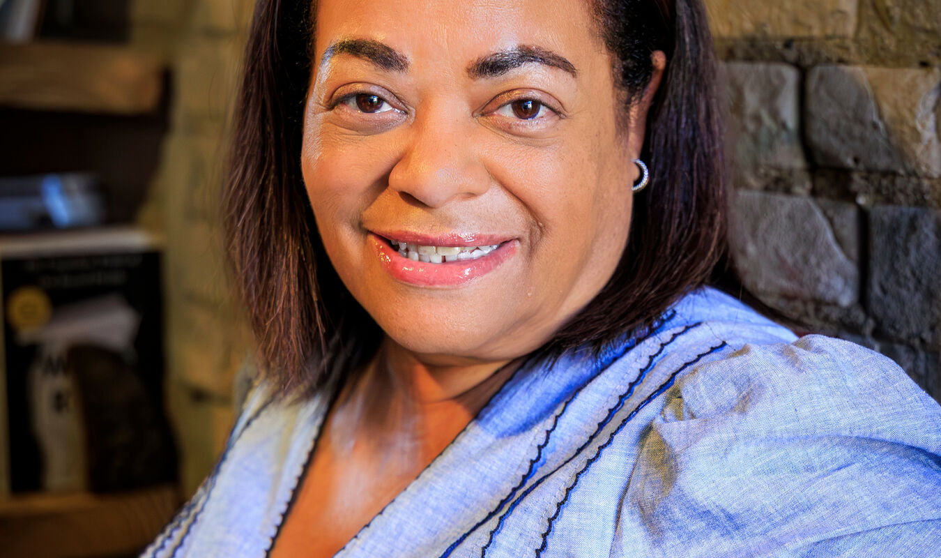 woman wearing a blue dress leaning next to a wall and smiling