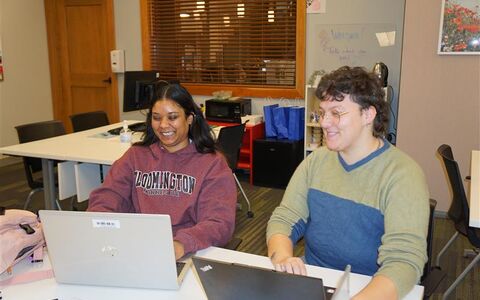 two people smiling sitting in front of laptops